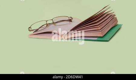 The glasses are lying on an open book on a solid green background Stock Photo