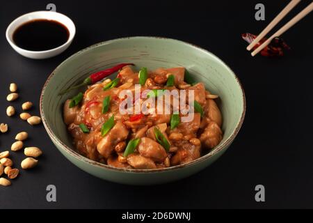 Kung Bao chicken on a black background. A Chinese dish with chicken, chili, peanuts, sauces and onions. Stock Photo