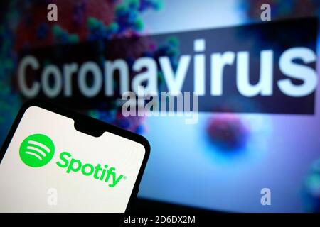 The Spotify logo seen displayed on a mobile phone with an illustrative model of the Coronavirus displayed on a monitor in the background. Stock Photo