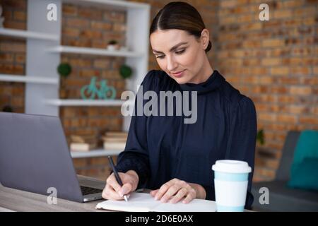 Woman taking notes while sitting on her desk Stock Photo