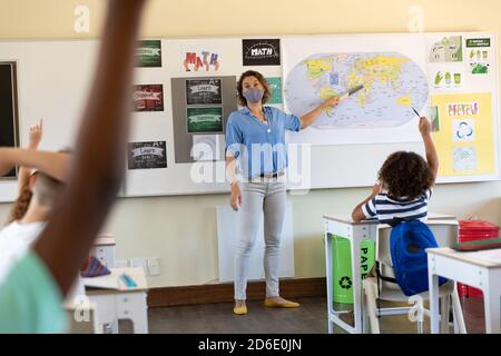 Female teacher wearing face mask teaching geography to students in class Stock Photo