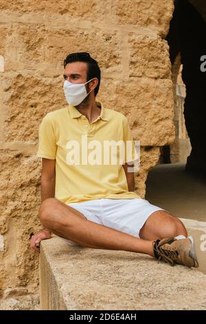 Vertical shot of a young Caucasian man in a mask sitting on a castle wall Stock Photo