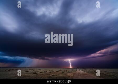 Distant thunderstorm lightning strike over a dirt road and field near Simla, Colorado, USA Stock Photo