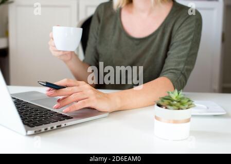 Blond hair young woman working at home on laptop. Woman sitting at the table at home working using computer laptop. Coronvirus concept. Stay home. Co Stock Photo