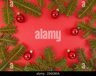 Christmas frame with fir tree branches and baubles on a red background. Festive flat lay with copy space inside. Stock photo. Stock Photo