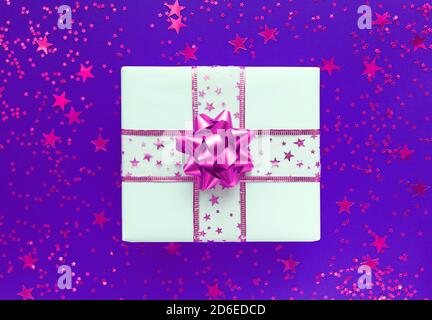 White gift box with pink bow and stars on a violet background. Stock Photo