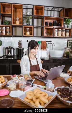 female chef wearing an apron while using a laptop while sitting in the kitchen Stock Photo