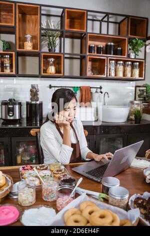 female chef unhappy wearing an apron when using a laptop while sitting in the kitchen Stock Photo