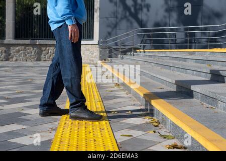 Man walking on yellow blocks of tactile paving for blind handicap.Braille blocks, tactile tiles for the visually impaired, Tenji blocks.Textured Stock Photo