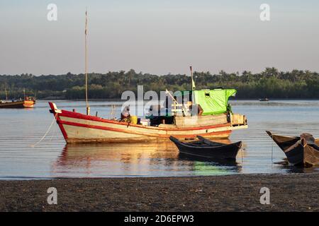 Chaung Thar, Myanmar - December 26, 2019: Traditional wooden boats by the shore of a river lit up by the sunset on December 26, 2019 in Chaung Thar Stock Photo