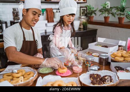 Father with little girl cooking making donuts together in kitchen Stock Photo