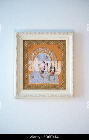 Framed orthodox religion decorated embroidered image. Virgin Mary and baby Jesus in white beads on orange background. White frame with ornaments. Hand Stock Photo