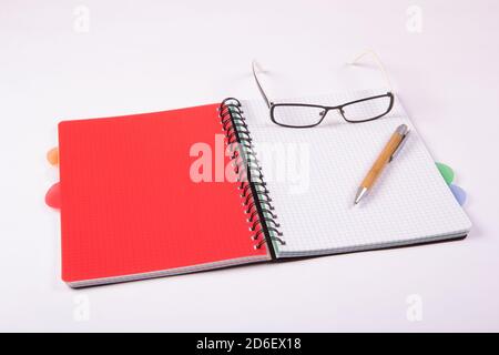 Open notebook with a pen and glasses on a light background. Notebook with a red card. Stock Photo