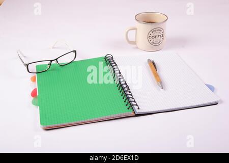 An open notebook with a pen, glasses and a cup of coffee on a light background. Green sheet notebook. Stock Photo