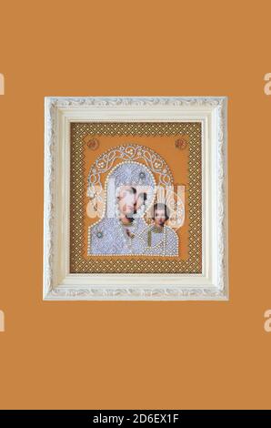 Framed orthodox religion decorated embroidered image. Virgin Mary and baby Jesus in white beads on orange background. White frame with ornaments. Hand Stock Photo