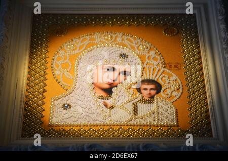 Framed orthodox religion decorated embroidered image. Virgin Mary and baby Jesus in white beads on orange background. White frame with ornaments. Hand Stock Photo