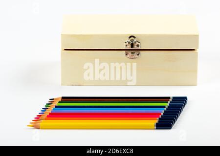 Stacked colored pencils next to a wooden box on a light background. Stock Photo