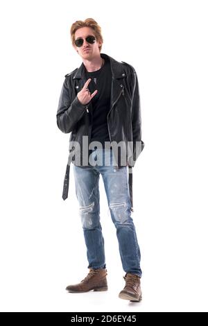Macho rocker man showing two finger horns or devil hand sign gesture in black leather jacket. Full body isolated on white background. Stock Photo