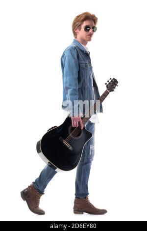 Profile view of redhead young man in jeans walking and carrying acoustic guitar. Full body isolated on white background. Stock Photo