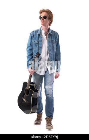 Cool macho stylish guitarist man walking looking away carrying acoustic guitar. Full body isolated on white background. Stock Photo