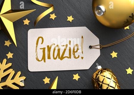 Christmas - Gift Tag with the Italian message 'Grazie!' (Thanks!) on a black stone background with gold colored christmas ornaments around. Stock Photo