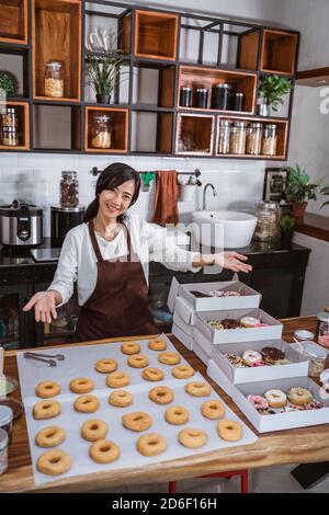 Young woman in a modern kitchen with a gesture serves the donuts that are on the table in the kitchen Stock Photo