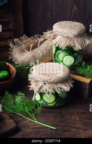 Jars with homemade pickled cucumbers cutted into slices with dill and garlic on rustic wooden background. Harvesting vegetables for the winter. Stock Photo