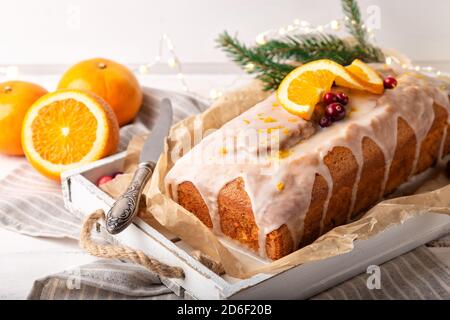 Christmas orange cake with cranberries and sugar icing on rustic wooden background. Holiday decoration with festoon and fir branch. Stock Photo