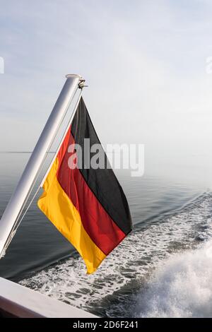 A German flag, waving in the wind, on a ship by the sea. Black, red, gold are the national colors. Icon image Stock Photo