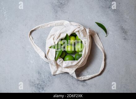 Ripe limes with fresh lime tree leaves in eco linen bag. top view. Stock Photo