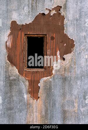 Black rectangular open window on wooden door with peeling paint Stock Photo
