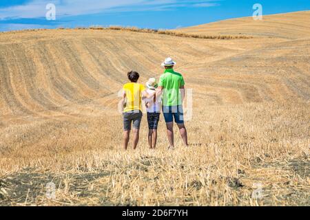 family, father, mother and young daughter from behind look at the hills in Val d'Orcia, Castiglione d'Orcia, province of Siena, Tuscany, Italy Stock Photo