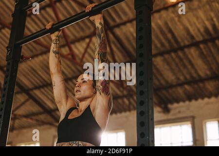 Woman doing pull up workout on horizontal bar. Strong female athlete performing pull ups inside old warehouse. Stock Photo