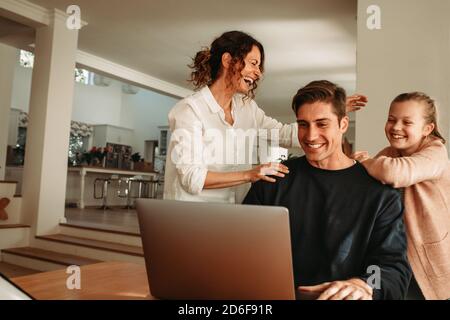 Man with his wife and daughter sitting in front of laptop making a video call. Happy family making video call while at home. Stock Photo
