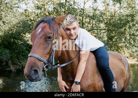 Portrait of a young blond man riding a horse over a river Stock Photo