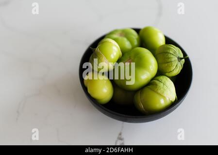 Bowl of fresh green tomatillo fruit on a white quartz counter. Stock Photo