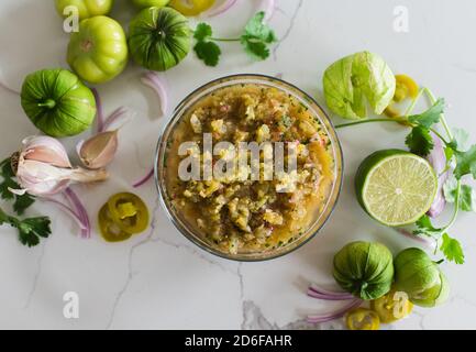 Overhead of tomatillo salsa and it's ingredients on white quartz. Stock Photo