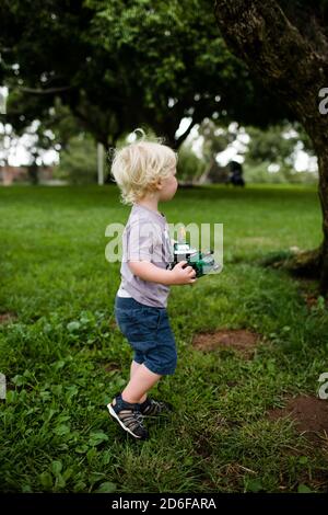 Two Year Old Holding Trucks Walking Through Park Stock Photo