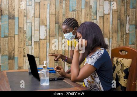 New normal - two young black female colleagues with face masks having a discussion Stock Photo