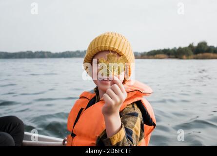 young boy on a fishing boat holding a maple leaf up looking happy Stock Photo