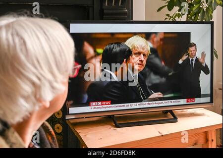 Televised news showing Boris Johnson in Parliament with text regarding rising unemployment during the Covid pandemic, watched by an older viewer. Stock Photo