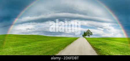 Country road in a green hilly landscape with a rainbow Stock Photo