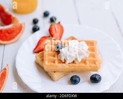 Healthy delicious Breakfast early in the morning. Fresh waffles whipped cream on top on a plate, blueberries, strawberries, grapefruit on the old whit Stock Photo