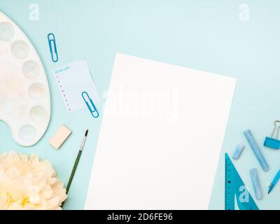 Back to school, education concept. Stationery, school tools near a white sheet of paper and painter brush besides isolated on blue color studio backgr Stock Photo
