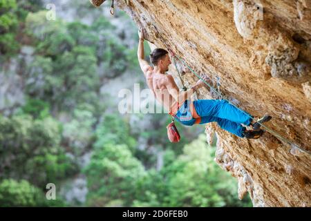 Rock climber on overhanging wall. Rock climbing on natural cliff. Strong young man trying hard to grip small handholds on challenging route. Stock Photo