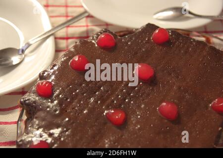 Closeup of a biscuit cake, decorated with a layer of chocolate and red cherries on top, ready to be served on the table Stock Photo