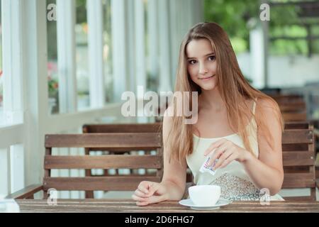 Woman adding a lot of sugar in a coffee or tea from a sugar bag, suggesting sugar overdose or unhealthy diet concept. Stock Photo
