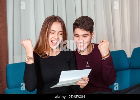 Excited amazed happy couple winners screaming with joy rejoicing reading good news holding mail paper letter celebrating taxes refund, cheap great off Stock Photo