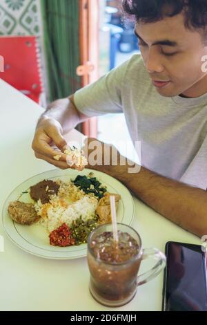 Man eating rice with sambar and vegetable curry from his tiffin box ...