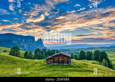 Hilly agricultural countryside with green pastures and a wooden house at Seiser Alm, Alpe di Siusi, the mountain Schlern, Sciliar, in the distance, at Stock Photo